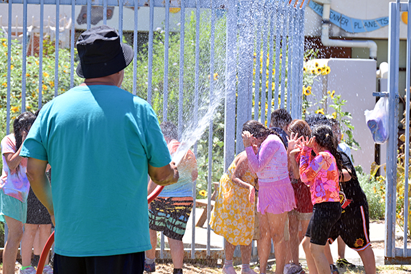 A man in a blue shirt and black bucket hat sprays students with water