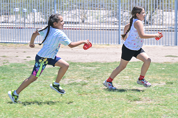 Two girls run across the field holding red cups of water