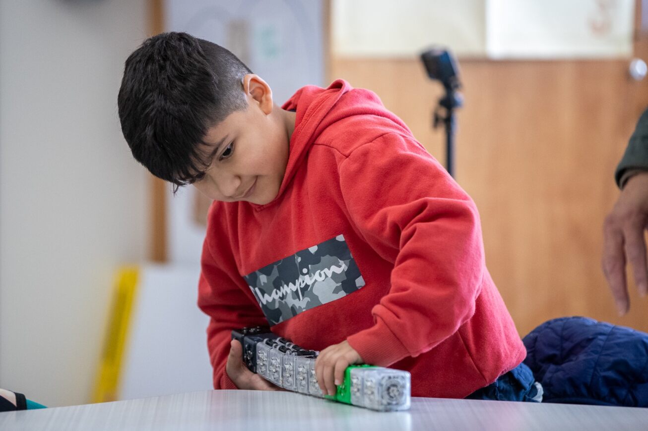 A boy in a red hoodie plays with a STEM block toy