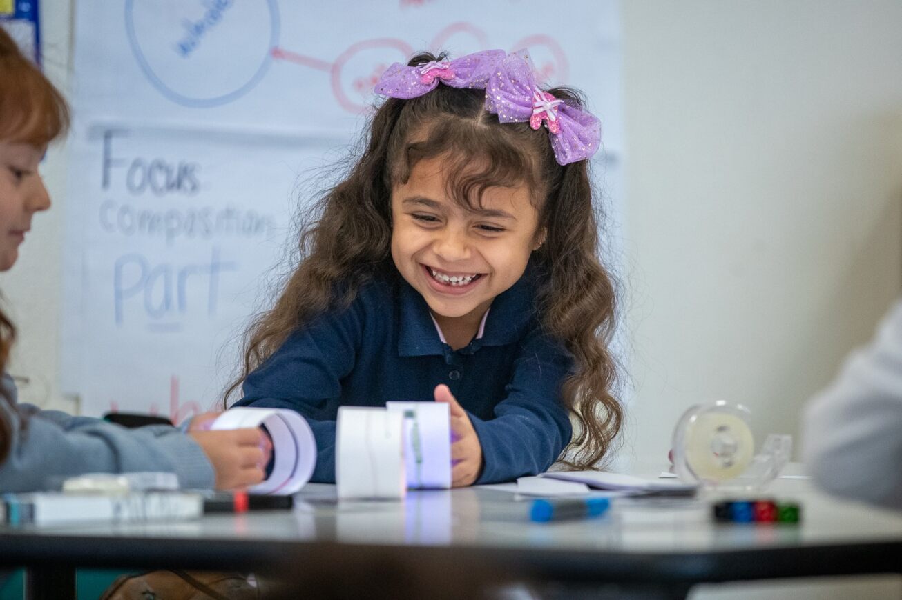 A girl with purple bows in her hair smiles while she plays with a STEM toy